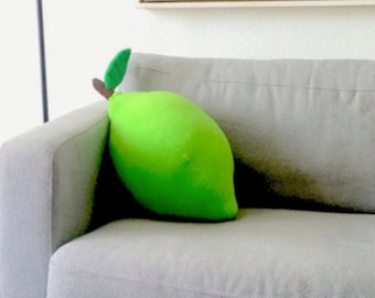 May include: Acoustic guitar on a stand next to a gray sofa with a lime-shaped pillow. A floor lamp with a yellow floral lampshade stands nearby. An abstract painting hangs on the wall.