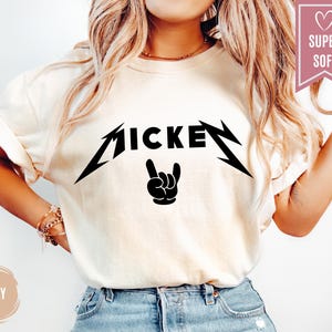 Pu&ograve; includere: T-shirt color avorio con una grafica nera che recita "MICKEY" in un font stilizzato, con un gesto della mano rock and roll. La maglietta ha maniche corte ed &egrave; realizzata in un materiale morbido.