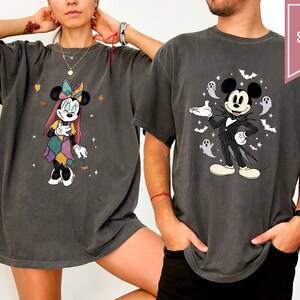 Puede incluir: Dos camisetas gris oscuro con personajes de Disney. Una camiseta muestra a Minnie Mouse con un vestido de retazos, la otra a Mickey Mouse con un traje de rayas con fantasmas y murci&eacute;lagos. Las camisetas tienen una etiqueta "SUPER SOFT" en forma de coraz&oacute;n.