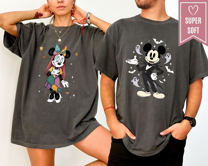 Puede incluir: Dos camisetas gris oscuro con personajes de Disney. Una camiseta muestra a Minnie Mouse con un vestido de retazos, la otra a Mickey Mouse con un traje de rayas con fantasmas y murci&eacute;lagos. Las camisetas tienen una etiqueta "SUPER SOFT" en forma de coraz&oacute;n.