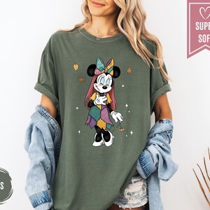 Puede incluir: Camiseta verde musgo con un gr&aacute;fico de Minnie Mouse en un dise&ntilde;o de patchwork. El gr&aacute;fico incluye un lazo, hojas de oto&ntilde;o y las palabras "Super Soft" en una pancarta rosa. La camiseta es de corte holgado.