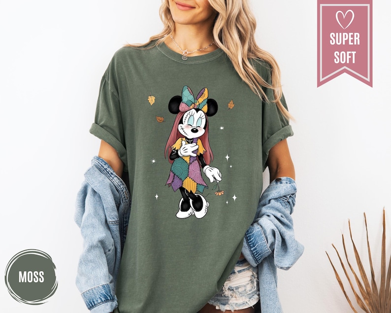 Puede incluir: Camiseta verde musgo con un gr&aacute;fico de Minnie Mouse en un dise&ntilde;o de patchwork. El gr&aacute;fico incluye un lazo, hojas de oto&ntilde;o y las palabras "Super Soft" en una pancarta rosa. La camiseta es de corte holgado.