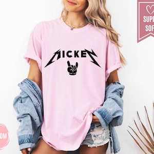 Pu&ograve; includere: T-shirt rosa chiaro con la scritta "MICKEY" in nero, con un carattere stilizzato e un gesto della mano rock and roll sotto. La maglietta ha maniche corte e una vestibilit&agrave; ampia.