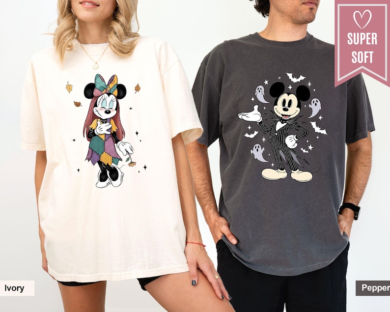 Puede incluir: Camisetas color marfil y pimienta con personajes de Disney. La camiseta marfil muestra a Minnie Mouse con un vestido de retazos, mientras que la camiseta pimienta muestra a Mickey Mouse con un atuendo inspirado en Jack Skellington, rodeado de fantasmas y murci&eacute;lagos.