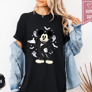 Puede incluir: Camiseta negra con un dise&ntilde;o de Halloween de Mickey Mouse como Jack Skellington, rodeado de murci&eacute;lagos y fantasmas. La camiseta tiene el texto "SUPER SOFT" en una pancarta rosa y "BLACK" en un c&iacute;rculo negro.