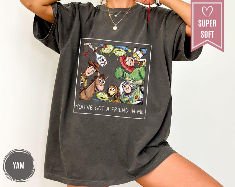 Op de afbeelding: Donkergrijs t-shirt met een kleurrijke afbeelding van personages uit de animatiefilm "Toy Story". De afbeelding is omlijst met de tekst "YOU'VE GOT A FRIEND IN ME" in het wit. Het shirt heeft een relaxte pasvorm en korte mouwen.