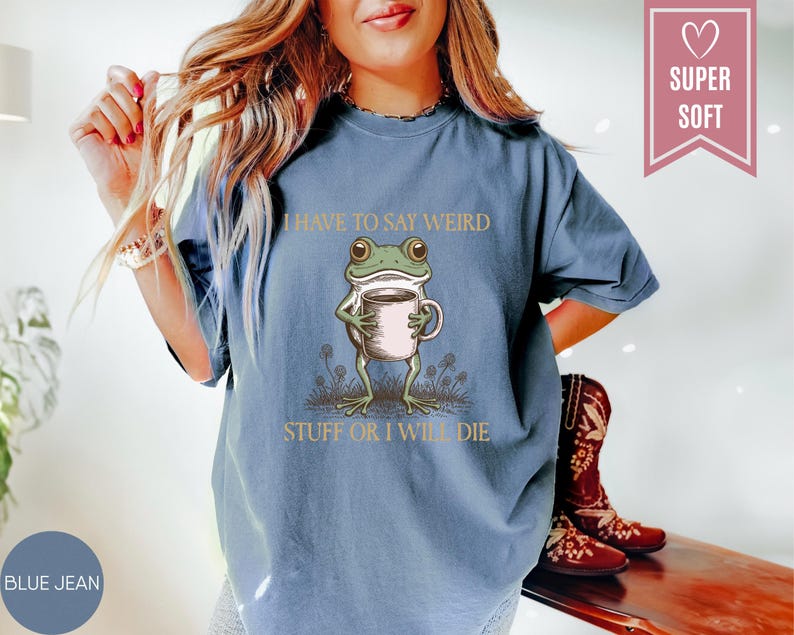 May include: Blue jean colored t-shirt with a graphic of a frog holding a coffee cup. The text on the shirt reads "I HAVE TO SAY WEIRD STUFF OR I WILL DIE". The shirt has a relaxed fit.