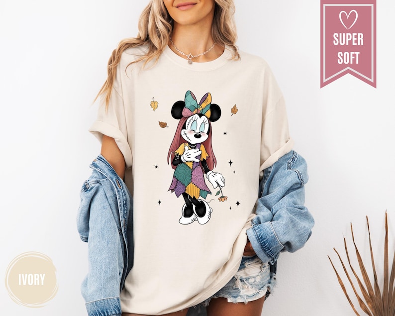Puede incluir: Camiseta de color marfil con un personaje de dibujos animados de Minnie Mouse con un vestido y lazo de patchwork. El dise&ntilde;o incluye hojas que caen y el texto "SUPER SOFT" en una pancarta rosa. La camiseta es parte de una colecci&oacute;n de ropa.
