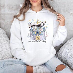 May include: White hoodie with a graphic of a pink castle with the text "Florida!! One Hell Of A Day" printed on the front.