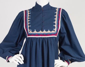 Könnte beinhalten: Ein marineblaues Midikleid mit langen Ärmeln und einem hohen Ausschnitt. Das Kleid hat einen bestickten Saum in Rot-, Beige- und Blautönen.