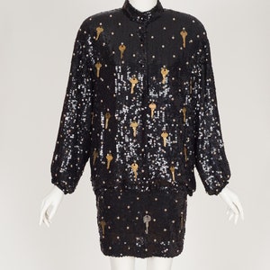 May include: A black sequined jacket and skirt set with gold key accents. The jacket has a mandarin collar and long sleeves. The skirt is a mini skirt.