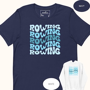 Puede incluir: Camiseta azul marino con la palabra "ROWING" repetida en una fuente ondulada de color azul claro. La camiseta tiene cuello redondo y mangas cortas. También se ve una sudadera con capucha blanca con el mismo diseño.