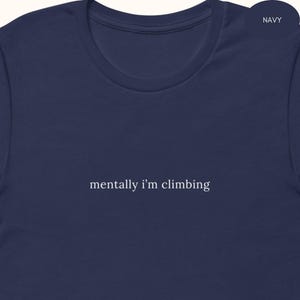 May include: Navy blue t-shirt with the text "mentally i'm climbing" in a simple, white font. The shirt has a crew neck and short sleeves. The word "NAVY" is in the upper right corner.