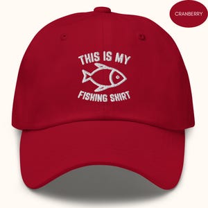 May include: A red baseball cap with white embroidery that reads "This is my fishing shirt" and a stylised fish graphic.