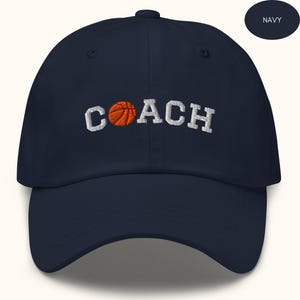 Könnte beinhalten: Marineblaue Baseballkappe mit weiß gesticktem Text "COACH" und einem Basketball-Motiv in der Mitte des Wortes.