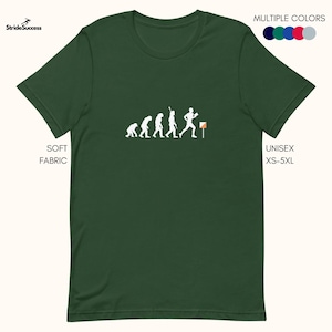 Può includere: Una maglietta verde con una silhouette bianca dell'evoluzione dell'uomo che termina con una persona che corre con una bussola. Il testo "SOFT FABRIC" è sul lato sinistro della maglietta e "UNISEX XS-5XL" è sul lato destro della maglietta. La maglietta è disponibile in diversi colori.