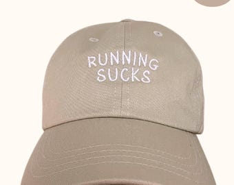 May include: A stone-colored baseball cap with the text "RUNNING SUCKS" embroidered in white on the front.