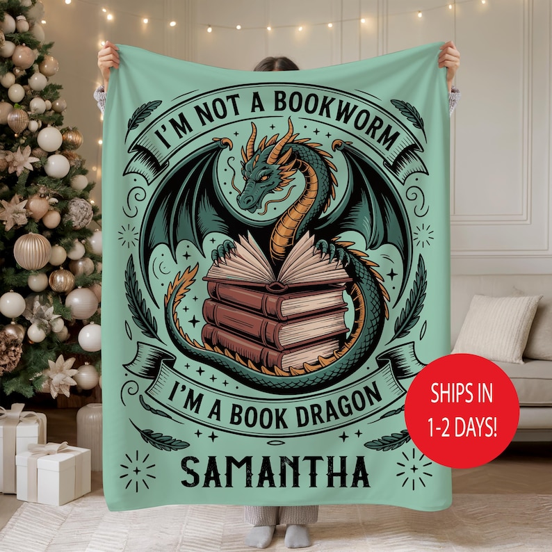 May include: A mint green blanket featuring a dragon illustration with the text "I'M NOT A BOOKWORM I'M A BOOK DRAGON" and the name "SAMANTHA". The dragon is green and black, with a stack of books. The blanket is held up by a person.
