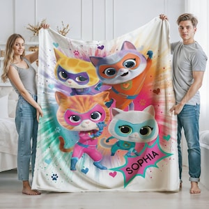May include: A white fleece blanket with a colorful design featuring four cartoon cats wearing superhero costumes. The cats are wearing masks and capes. The blanket has a green and blue swirl design and the words "Sophia" in a pink circle.