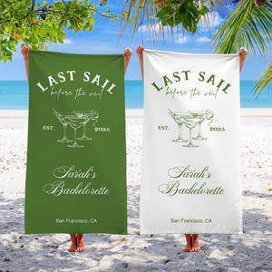 May include: Two green and white beach towels with the text "Last Sail Before the Veil" and "Sarah's Bachelorette" with a graphic of three martini glasses. The towels are hanging on a beach.