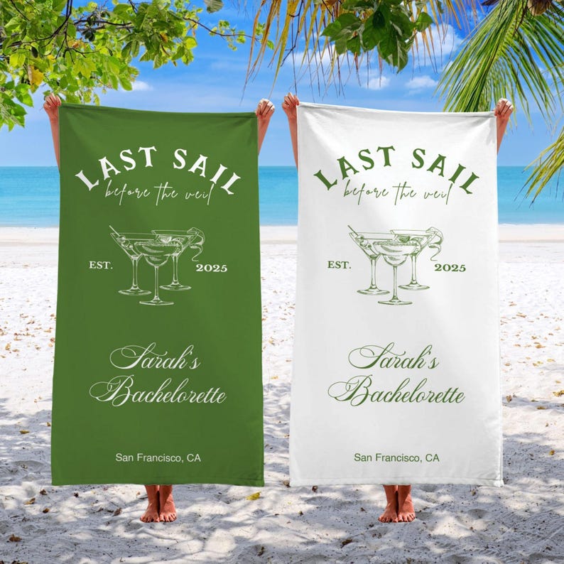 May include: Two green and white beach towels with the text "Last Sail Before the Veil" and "Sarah's Bachelorette" with a graphic of three martini glasses. The towels are hanging on a beach.