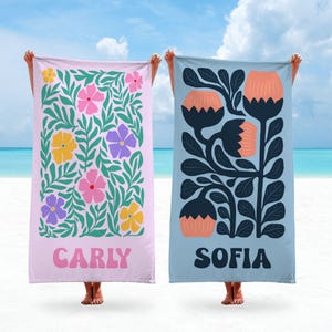 May include: Two pink and blue beach towels with floral patterns and personalized names. The pink towel has a green floral pattern with yellow, pink, and purple flowers and the name "Carly" printed on the bottom. The blue towel has a dark blue floral pattern with orange flowers and the name "Sofia" printed on the bottom.