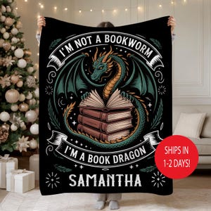 May include: Black blanket with a dragon design. The dragon is green and gold, with wings spread over a stack of books. Text reads "I'M NOT A BOOKWORM I'M A BOOK DRAGON" and "SAMANTHA". Decorative blanket.