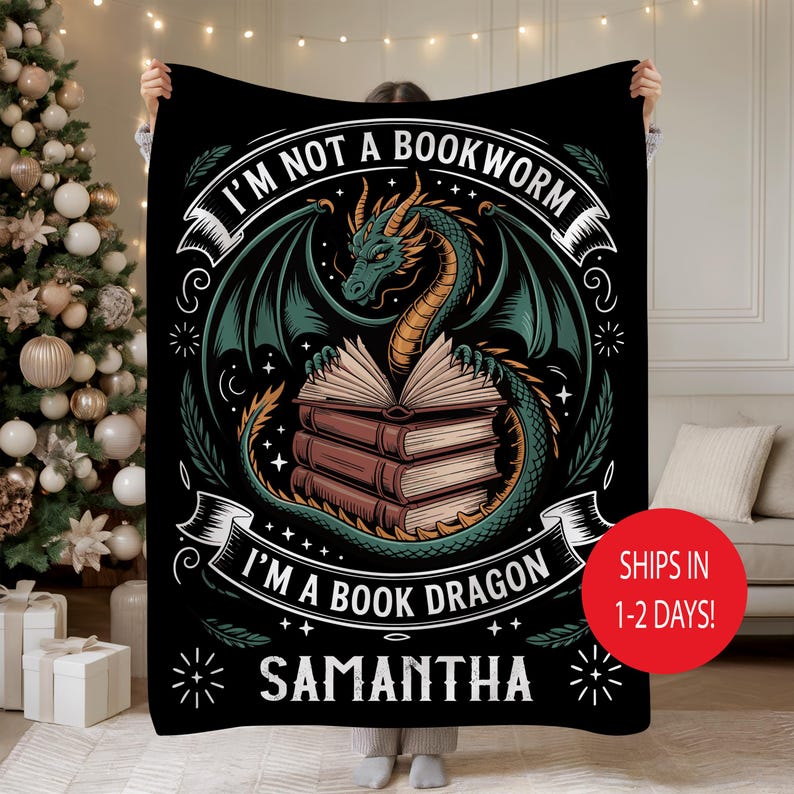 May include: Black blanket with a dragon design. The dragon is green and gold, with wings spread over a stack of books. Text reads "I'M NOT A BOOKWORM I'M A BOOK DRAGON" and "SAMANTHA". Decorative blanket.