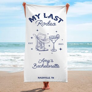 Pu&ograve; includere: Asciugamano da spiaggia bianco con testo blu che recita "My Last Rodeo Est 2025 Amy's Bachelorette Nashville, TN". L'asciugamano presenta anche un disegno di un cappello da cowboy, stivali e un bicchiere di margarita.