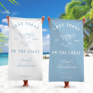 May include: Two white beach towels with blue text and a blue martini glass graphic. The text reads "Last Toast Est. 2025 On The Coast Sarah's Bachelorette San Francisco, CA". One towel is white and the other is light blue.