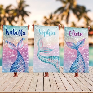 May include: Three mermaid tail beach towels with personalized names: Isabella, Sophia, and Olivia. The towels feature a blue and pink mermaid tail with iridescent scales against a sparkly background.