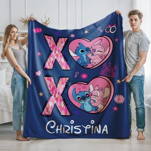 May include: Blue fleece blanket with a pink and white XO design, featuring Stitch and Angel from Lilo & Stitch. The blanket has a pink heart with the characters kissing and the name "Christina" printed on the bottom.