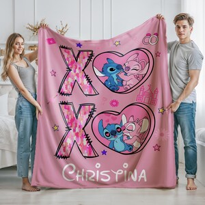 May include: Pink fleece blanket with a pink and white patterned X and a pink and white patterned O. The blanket features two hearts with Stitch and Angel from Lilo & Stitch kissing. The text "CHRISTINA" is printed on the blanket.