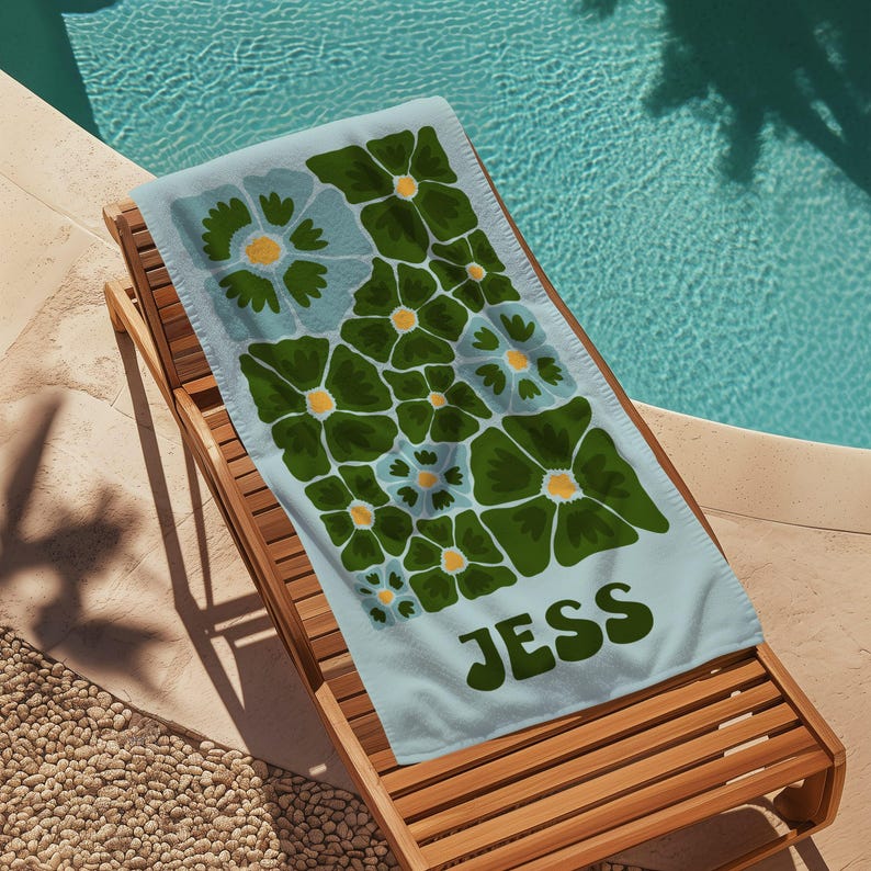 May include: A light blue beach towel with a floral pattern in shades of green and blue. The towel has the name "Jess" printed in green letters.