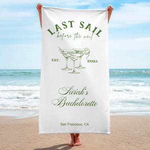 May include: White beach towel with green text that reads "Last Sail Before the Veil" and "Sarah's Bachelorette" with a drawing of three martini glasses. The text also includes "Est. 2025" and "San Francisco, CA".