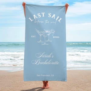 May include: Light blue beach towel with the text "Last Sail Before the Veil" and a graphic of three martini glasses. The text "Sarah's Bachelorette" is below the glasses, and the text "San Francisco, CA" is at the bottom of the towel.