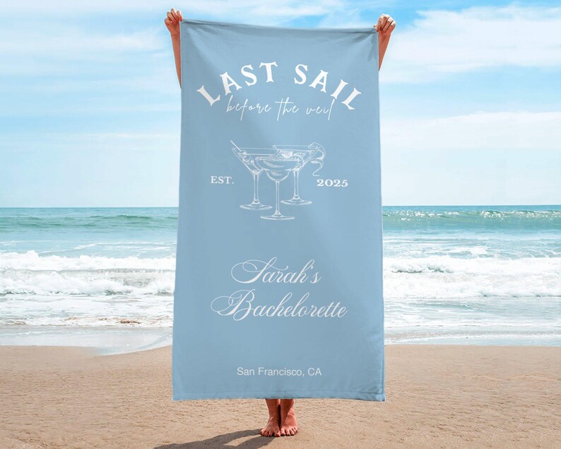 May include: Light blue beach towel with the text "Last Sail Before the Veil" and a graphic of three martini glasses. The text "Sarah's Bachelorette" is below the glasses, and the text "San Francisco, CA" is at the bottom of the towel.