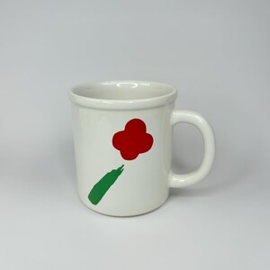 Pode incluir: Caneca de cer&acirc;mica branca com um desenho de flor vermelha e caule verde.