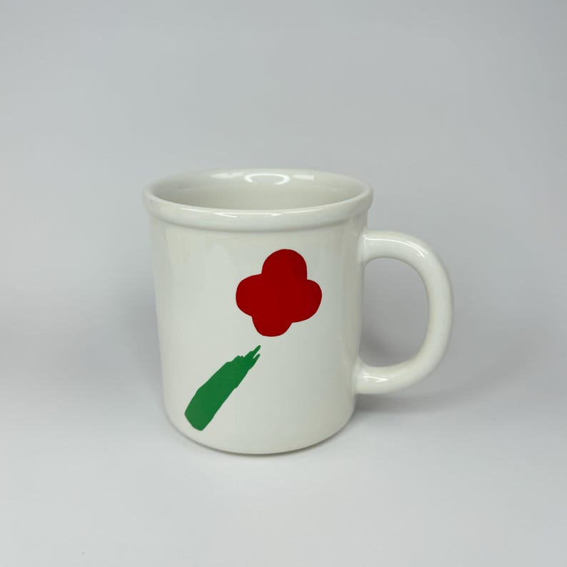 Pode incluir: Caneca de cer&acirc;mica branca com um desenho de flor vermelha e caule verde.