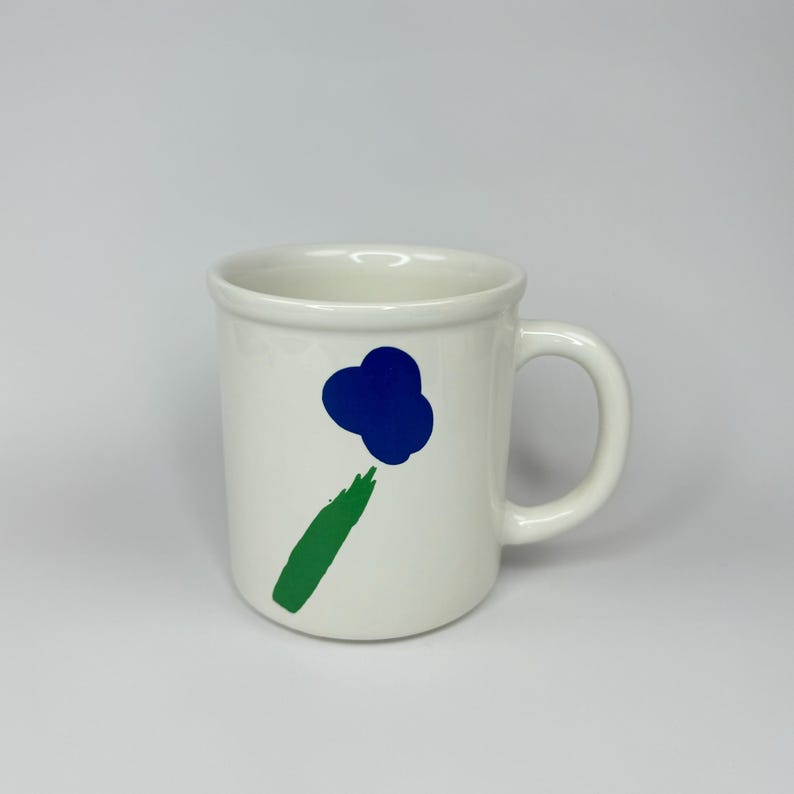 Pode incluir: Caneca de cer&acirc;mica branca com um design abstrato de flor em azul e verde.
