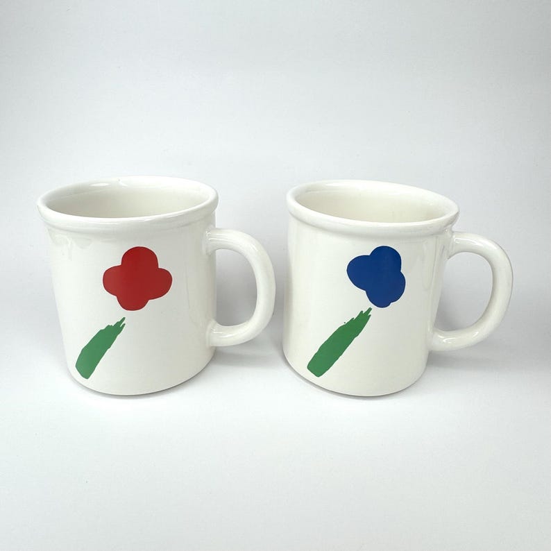 Pode incluir: Duas canecas de cer&acirc;mica branca com desenhos abstratos de flores verdes, vermelhas e azuis.
