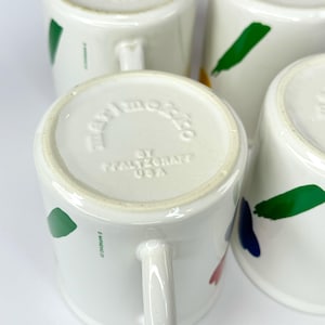 Pode incluir: Close-up da parte inferior de uma caneca de cer&acirc;mica branca com um design abstrato em verde, azul, vermelho e amarelo. A caneca &eacute; marcada com "Hallmark Co. by Hallmark USA".