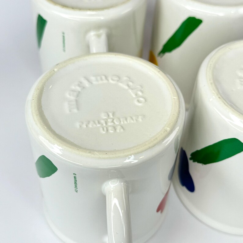 Pode incluir: Close-up da parte inferior de uma caneca de cer&acirc;mica branca com um design abstrato em verde, azul, vermelho e amarelo. A caneca &eacute; marcada com "Hallmark Co. by Hallmark USA".