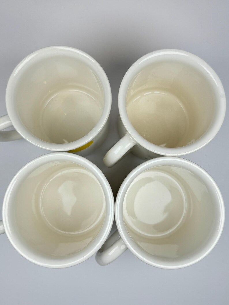 Pode incluir: Quatro canecas de cer&acirc;mica branca com um design amarelo na parte inferior. As canecas est&atilde;o vazias e est&atilde;o dispostas em c&iacute;rculo.