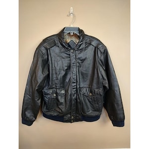 May include: Black leather bomber jacket with a collared neckline, two front pockets, and a ribbed navy blue hem and cuffs. The jacket is hanging on a hanger against a neutral background. The jacket has a quilted lining.