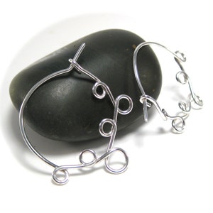 May include: A pair of silver hoop earrings with a delicate, intricate design. The earrings are made of thin wire that is twisted and looped to create a unique and stylish look.