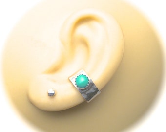 May include: A silver ear cuff with a turquoise-colored stone and a small silver stud earring. The ear cuff is rectangular with a hammered texture and a scalloped edge around the stone. The turquoise stone is round and set in the center of the cuff.