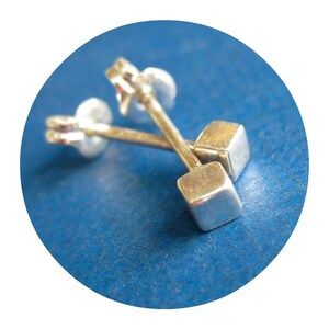 May include: A pair of silver cube stud earrings on a blue background.