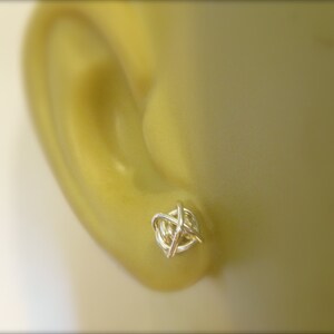 May include: Silver wire knot earrings. The earrings are small and delicate, and they are a great way to add a touch of style to any outfit.