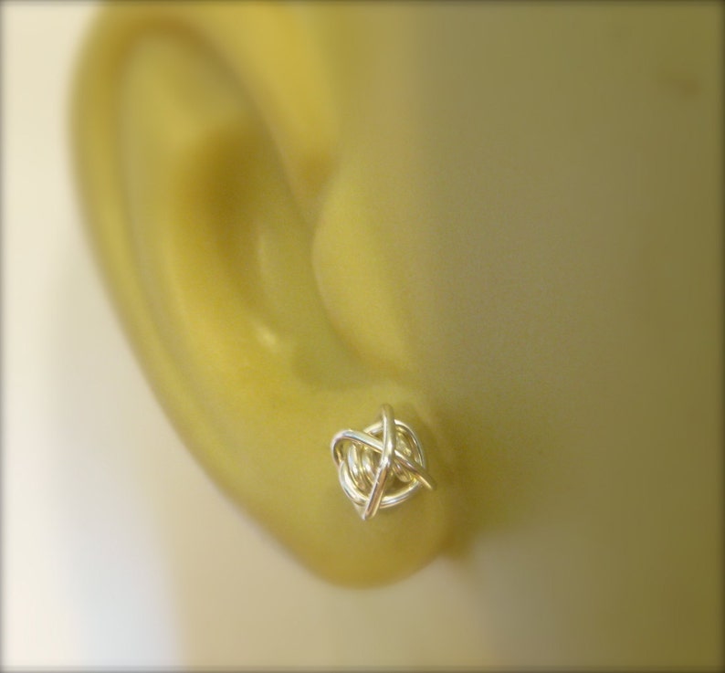 May include: Silver wire knot earrings. The earrings are small and delicate, and they are a great way to add a touch of style to any outfit.